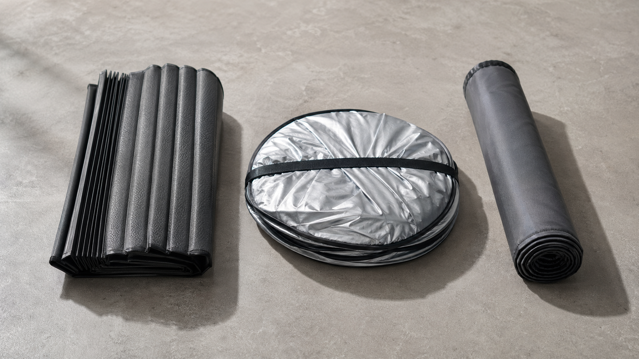 Three folded shades stacked on a walnut desk: rectangular, circular spring-fold, rolled tube