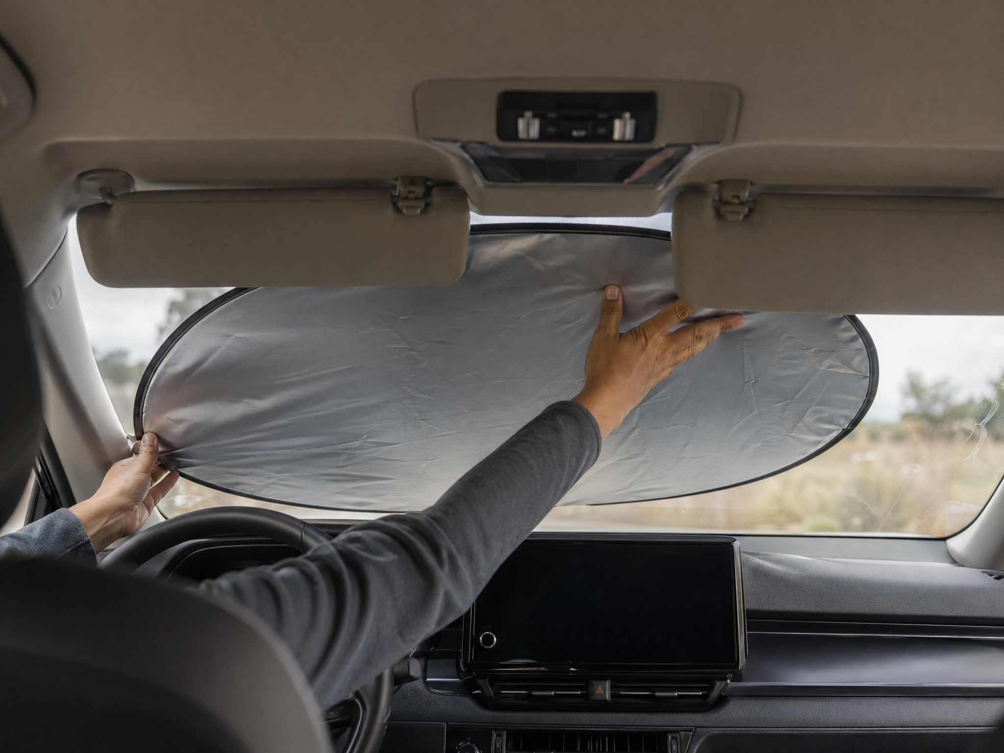 Hands installing a folded sunshade in a 2024 Toyota Camry, lower-left corner catching the A-pillar trim
